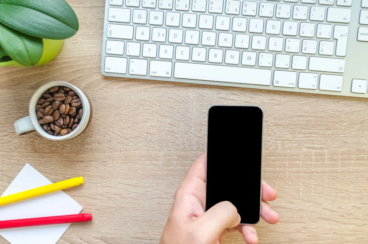 dłoń trzymająca smartfon na drewnianym biurku obok klawiatury — Ulefone Armor 24 w zgłoszeniu — jak odpowiadamy i co radzimy