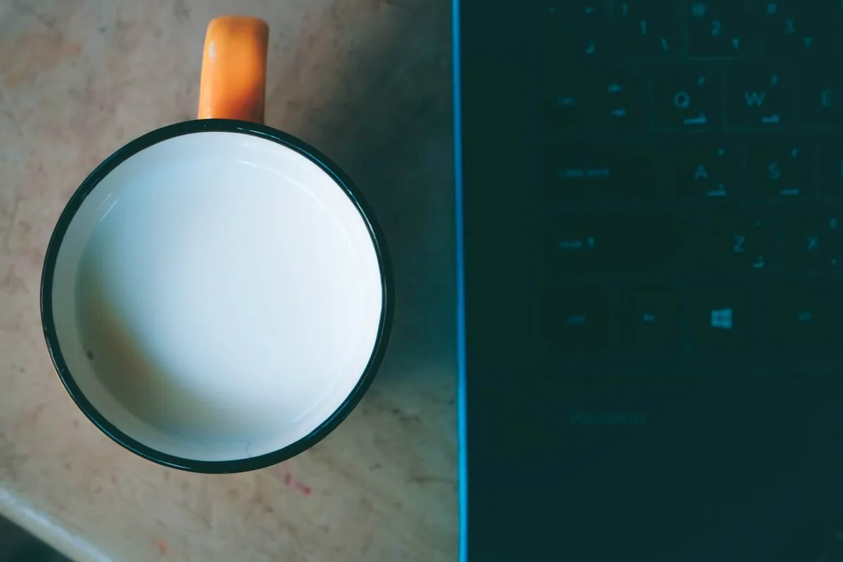 Kubek z mlekiem stojący tuż obok otwartego laptopa z klawiaturą