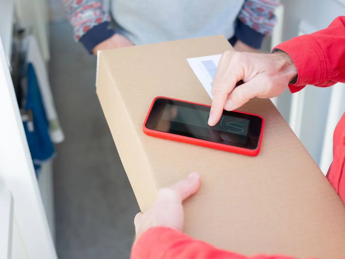 A person signs a package delivery confirmation using a smartphone, showcasing contact-free delivery.