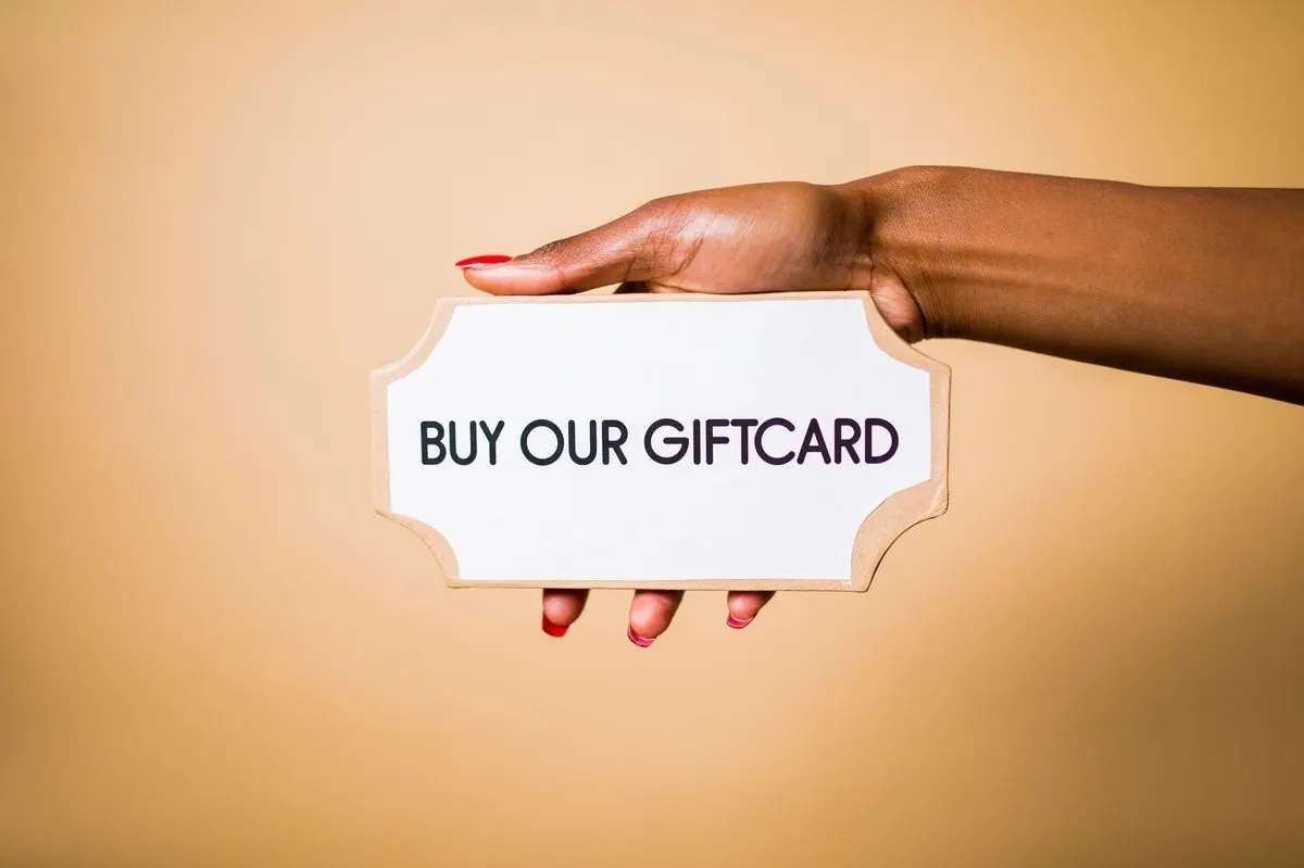 Dłoń trzymająca tabliczkę z napisem Buy our giftcard — Subiekt GT — obsługa voucherów i kart podarunkowych