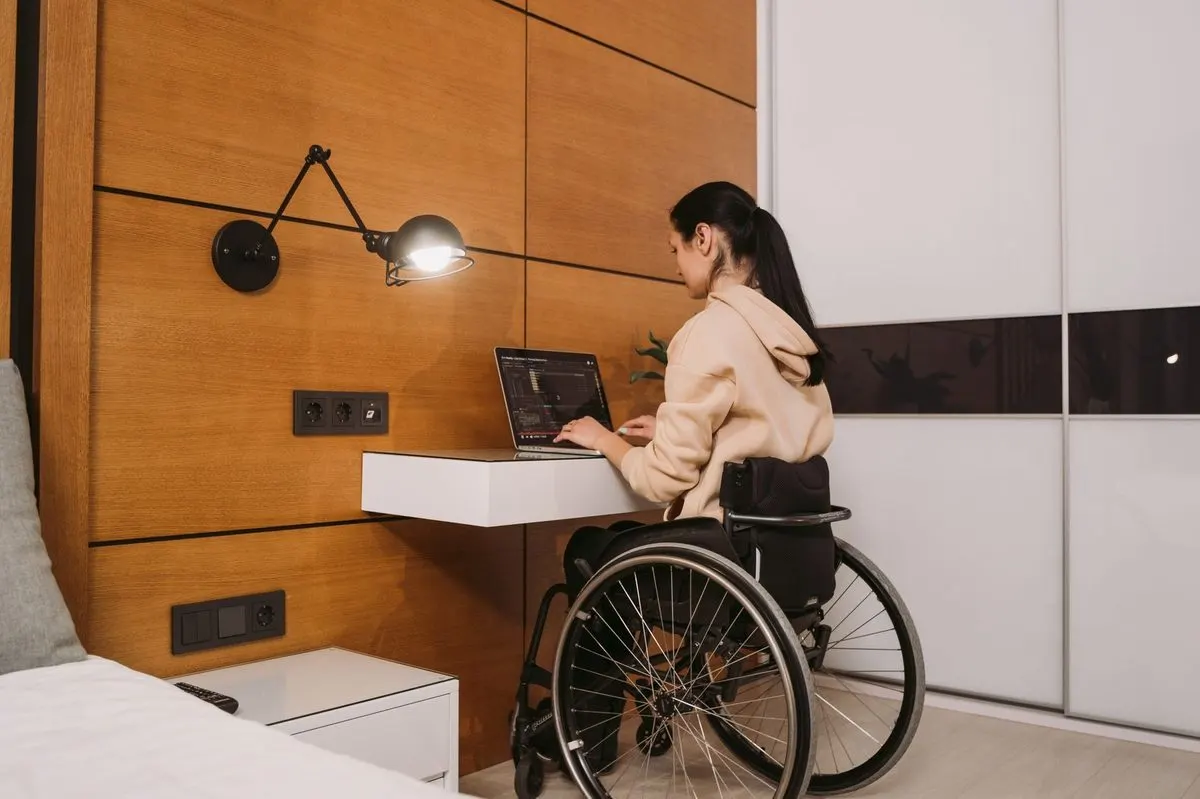 Osoba na wózku inwalidzkim pracująca przy laptopie, widok od tyłu — Zgłoszenie od osoby z ograniczoną mobilnością — dostosowanie wizyty