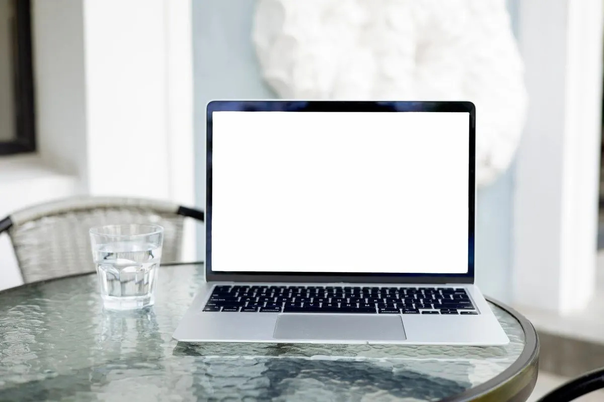 Laptop z pustym ekranem na stoliku kawiarnianym, obok szklanka wody — Jak bezpiecznie korzystać z publicznego Wi-Fi