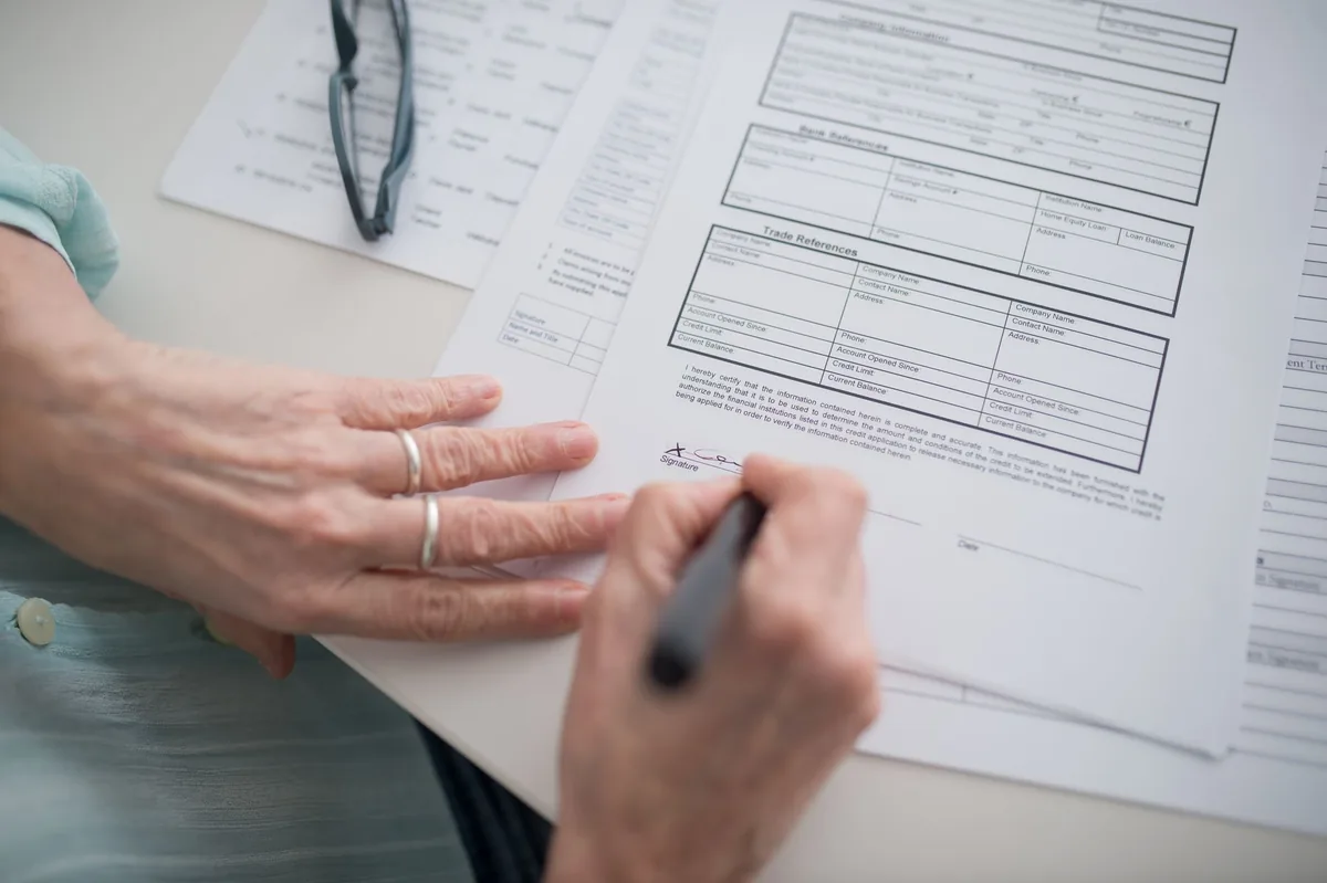 A close-up view of a hand signing official documents with a pen indoors.
