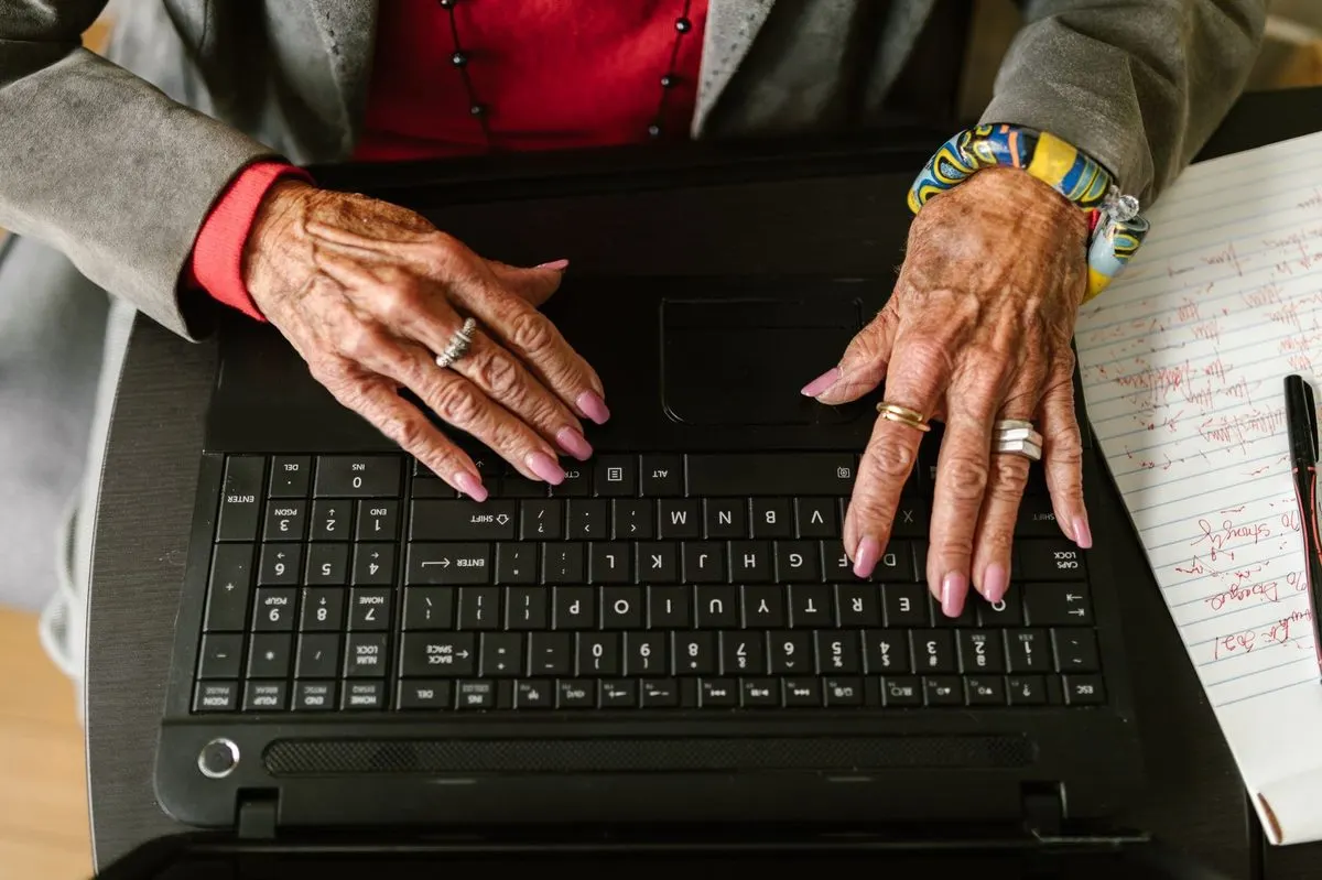 Starsze dłonie na klawiaturze laptopa obok notatnika — Senior zgubił się w obsłudze komputera i potrzebuje szybkiej pomocy