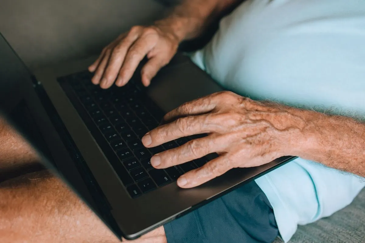 Starsze dłonie na klawiaturze laptopa — Zgłoszenie awarii komputera seniora przez osobę bliską