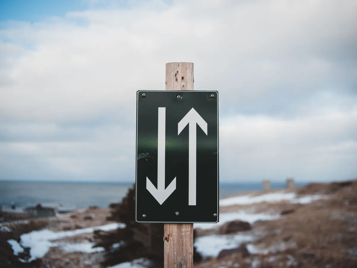 Sign of two way trail on sandy shore of calm sea with snow under cloudy sky on winter day