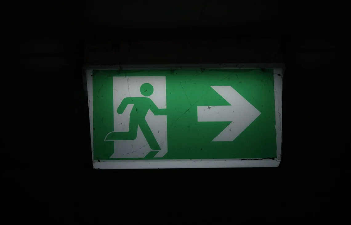 Illuminated green emergency exit sign with an arrow pointing right in a dark setting.