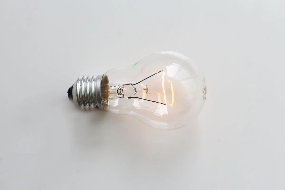 A close-up of an illuminated incandescent light bulb against a white background.