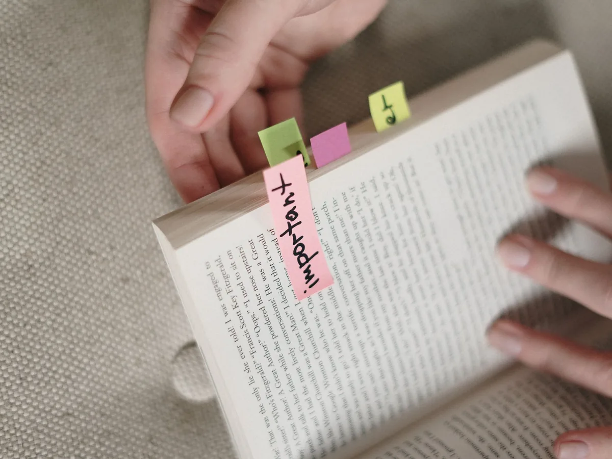 Hands holding a book with colorful sticky notes marking important pages.