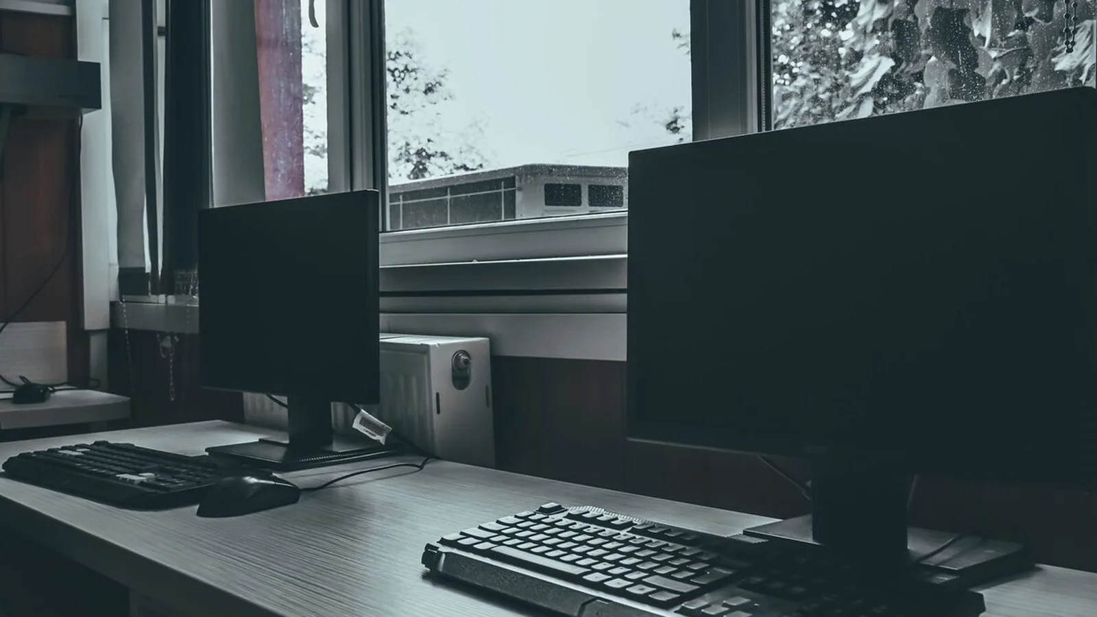 Stanowisko pracy z dwoma monitorami i klawiaturą przy oknie