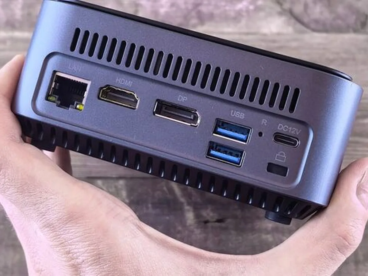 Mały komputer typu mini PC trzymany w dłoni z widocznymi portami