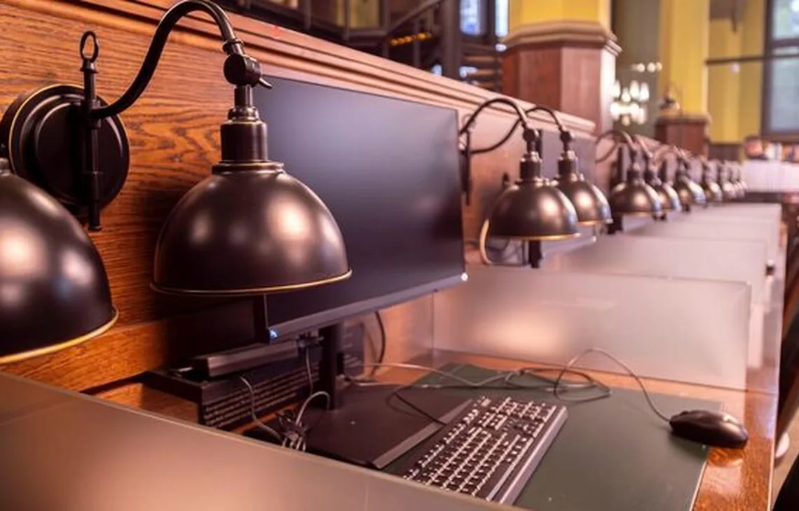 Rząd stanowisk komputerowych z lampami w czytelni biblioteki