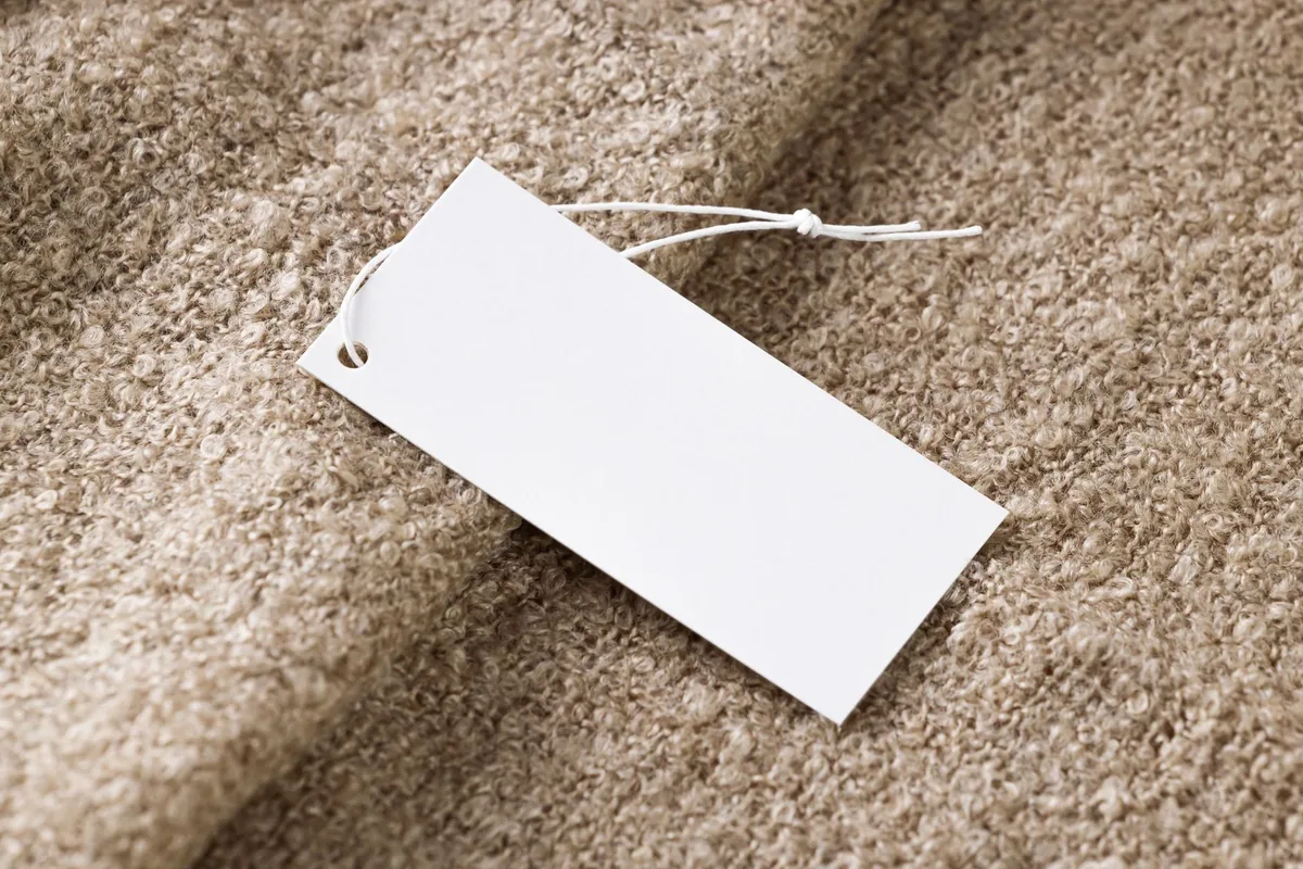 Close-up of a blank white price tag on textured beige fabric, ideal for branding use.
