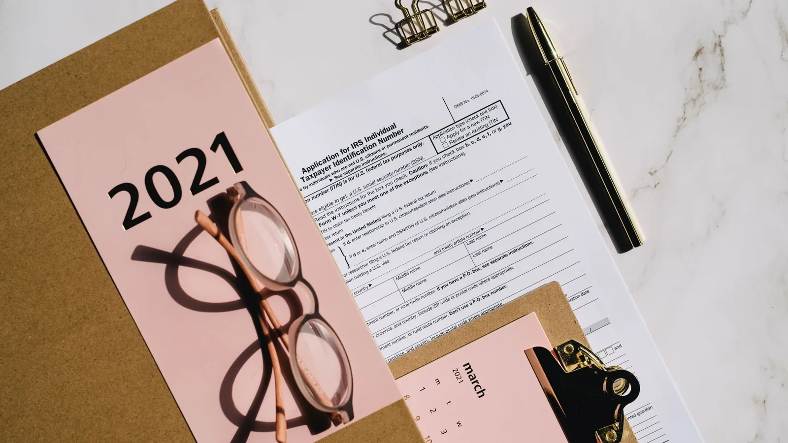 Flat lay of 2021 tax documents with glasses, pen, and calendar on a desk.