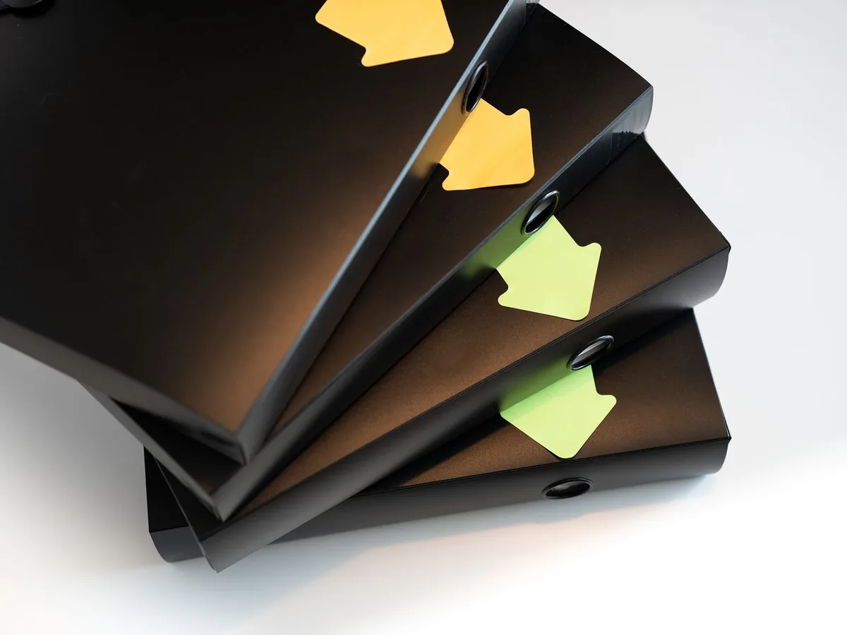 A stack of black ring binders with yellow and green labels for organization.