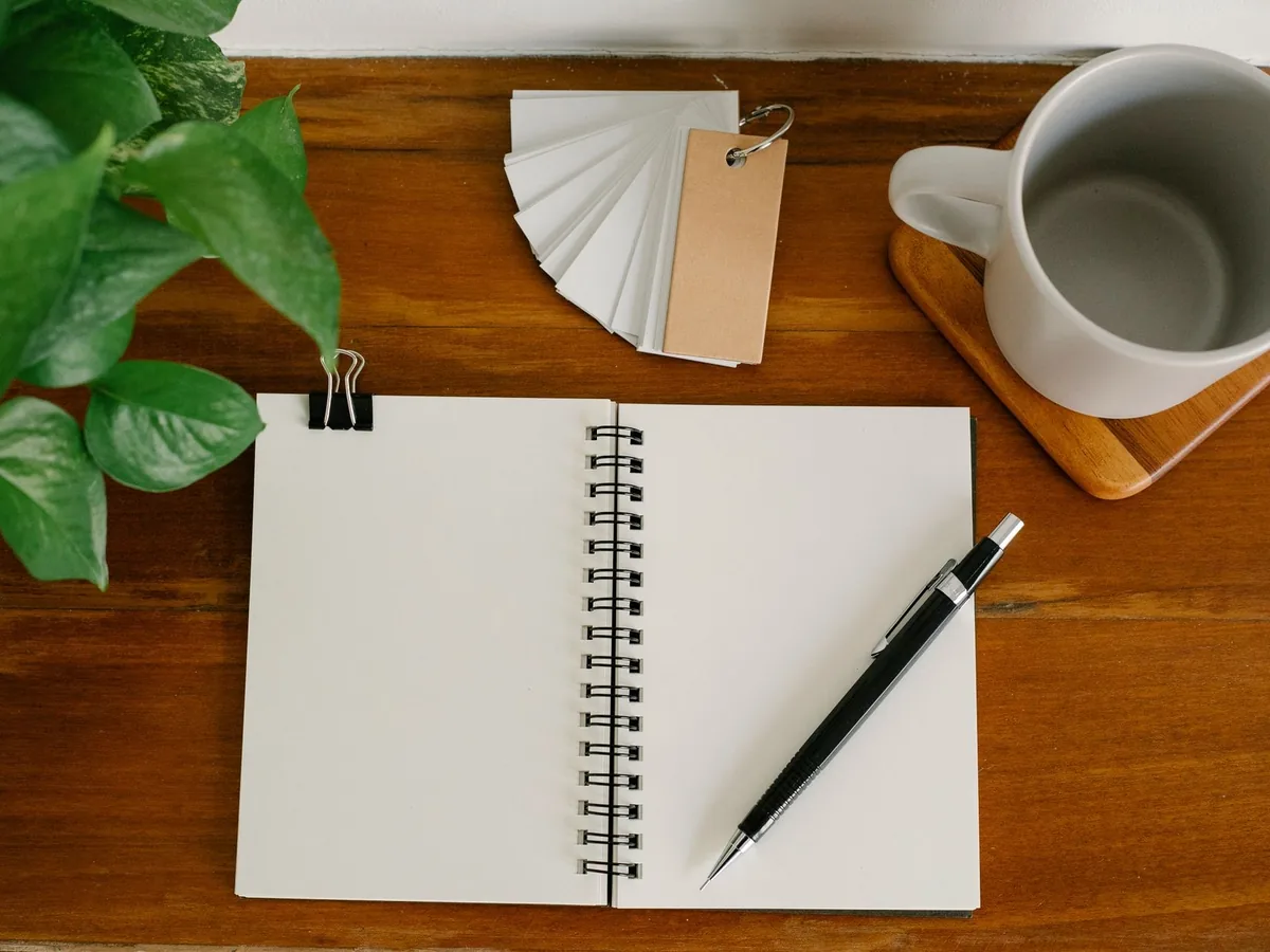 From above empty notebook with pen and tags placed near potted plant and empty mug on office table