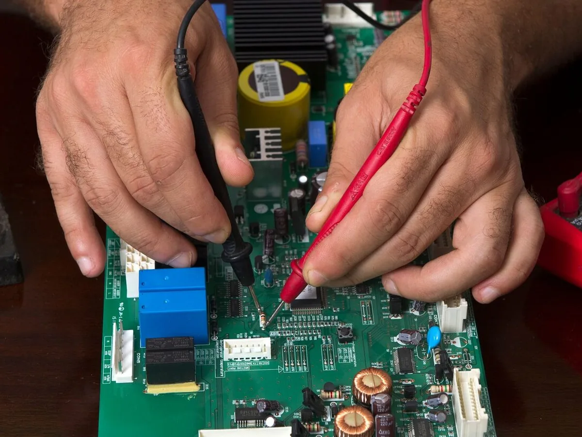 Dłonie z sondami multimetru testujące zieloną płytkę elektroniczną