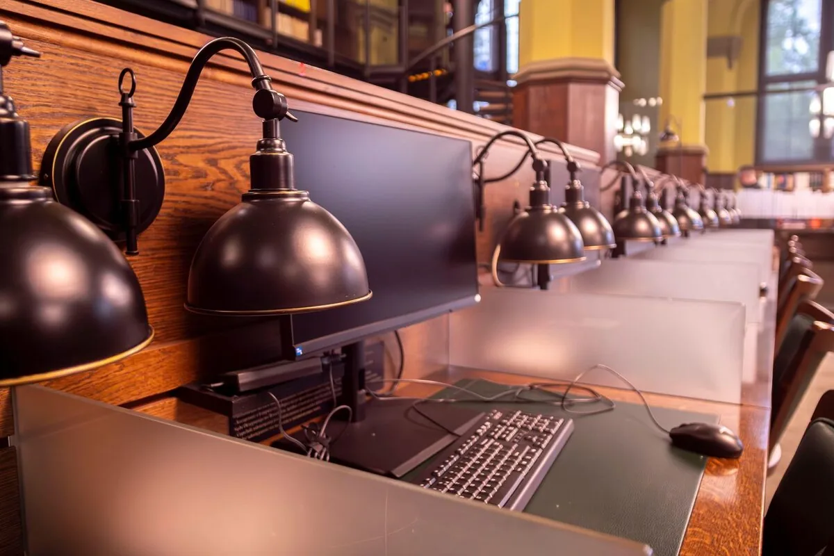 Rząd stanowisk komputerowych z lampami w czytelni biblioteki