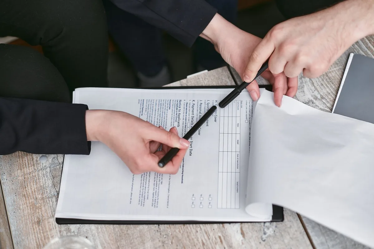 Close-up of business hands finalizing agreement with pen on documents.