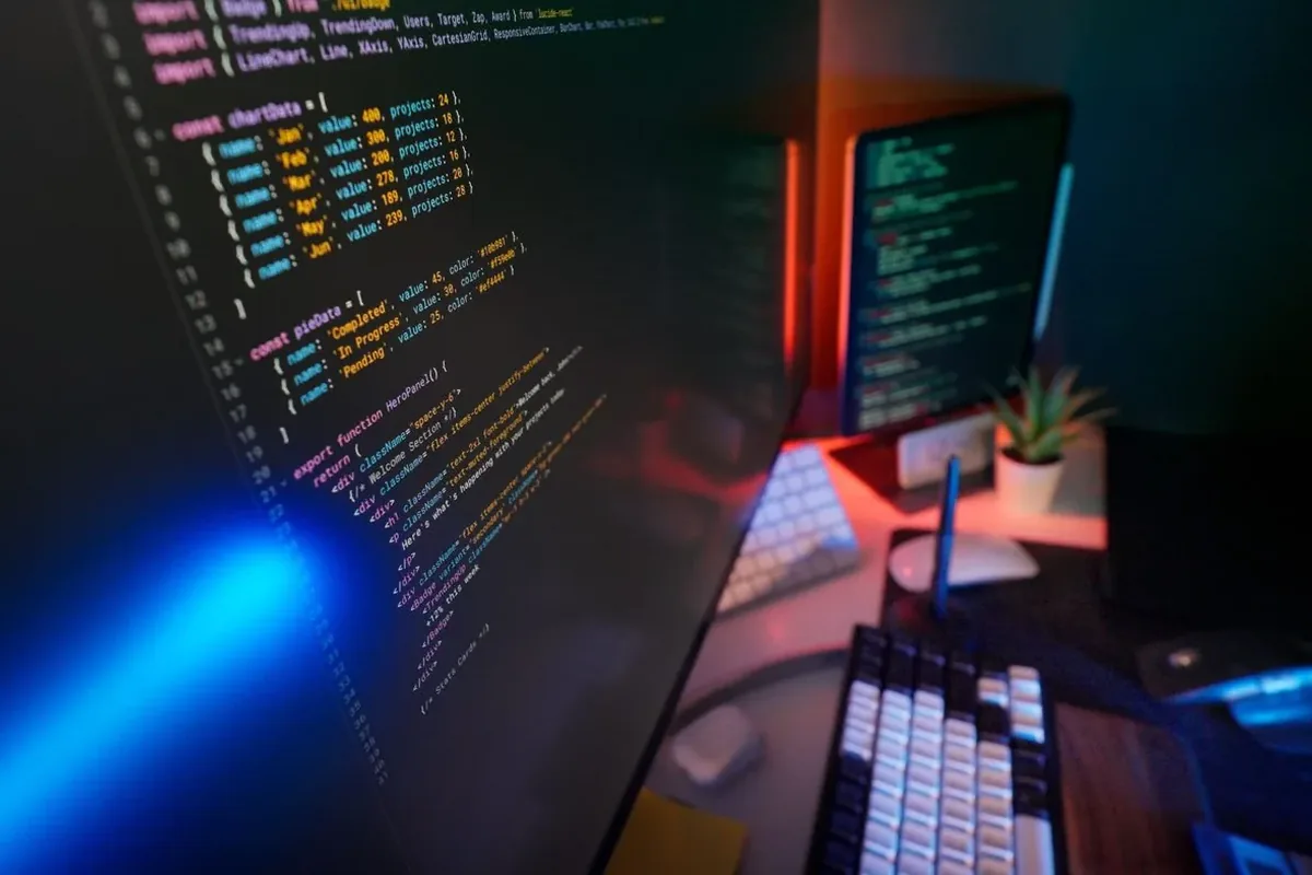 Kod programistyczny na ekranach komputera przy biurku ze stacją dokującą
