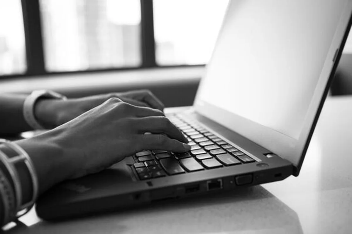 Czarno-białe zdjęcie dłoni piszących na klawiaturze laptopa