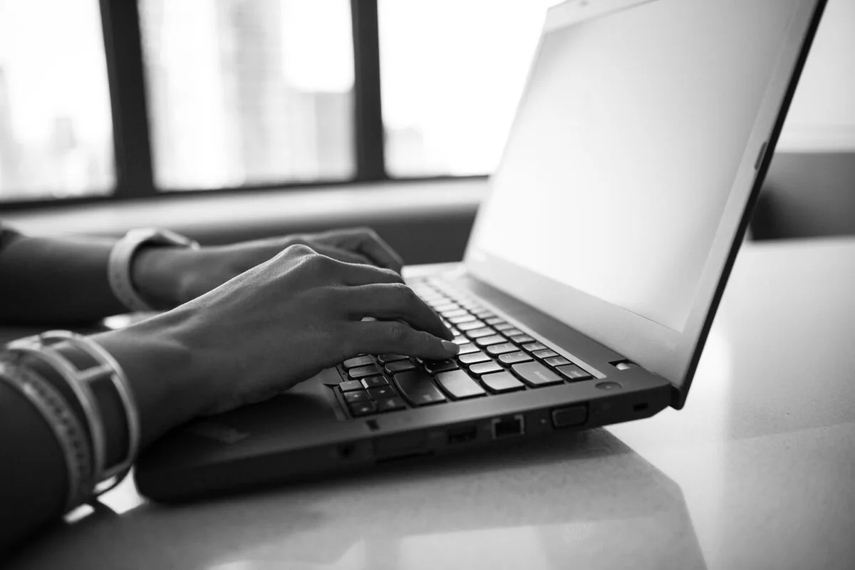 Czarno-białe zdjęcie dłoni piszących na klawiaturze laptopa