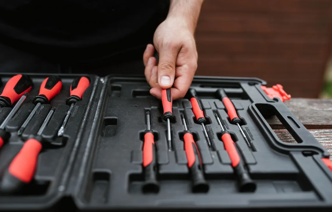 From above of crop anonymous skillful male in casual clothes choosing screwdriver from toolbox in daylight