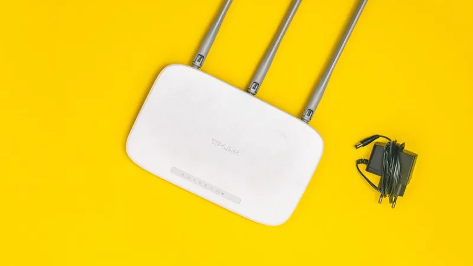 Biały router WiFi z trzema antenami i zasilaczem na żółtym tle