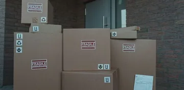 Stos kartonowych pudeł z naklejkami FRAGILE przed drzwiami wejściowymi