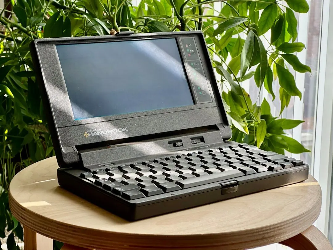 Zabytkowy laptop Gateway 2000 Handbook stojący na stoliku wśród roślin — Naprawa sprzętu w domach jednorodzinnych na przedmieściach Warszawy