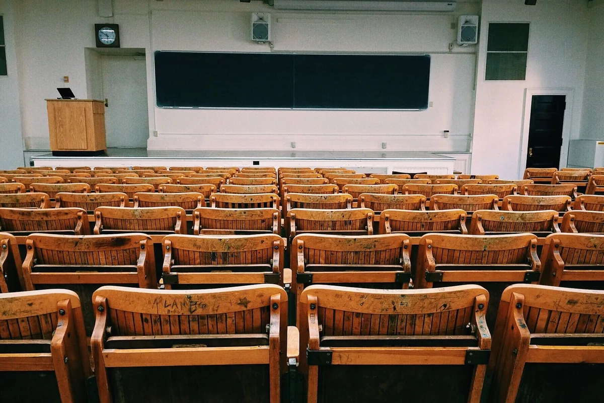 An empty lecture hall featuring wooden chairs and a large blackboard.