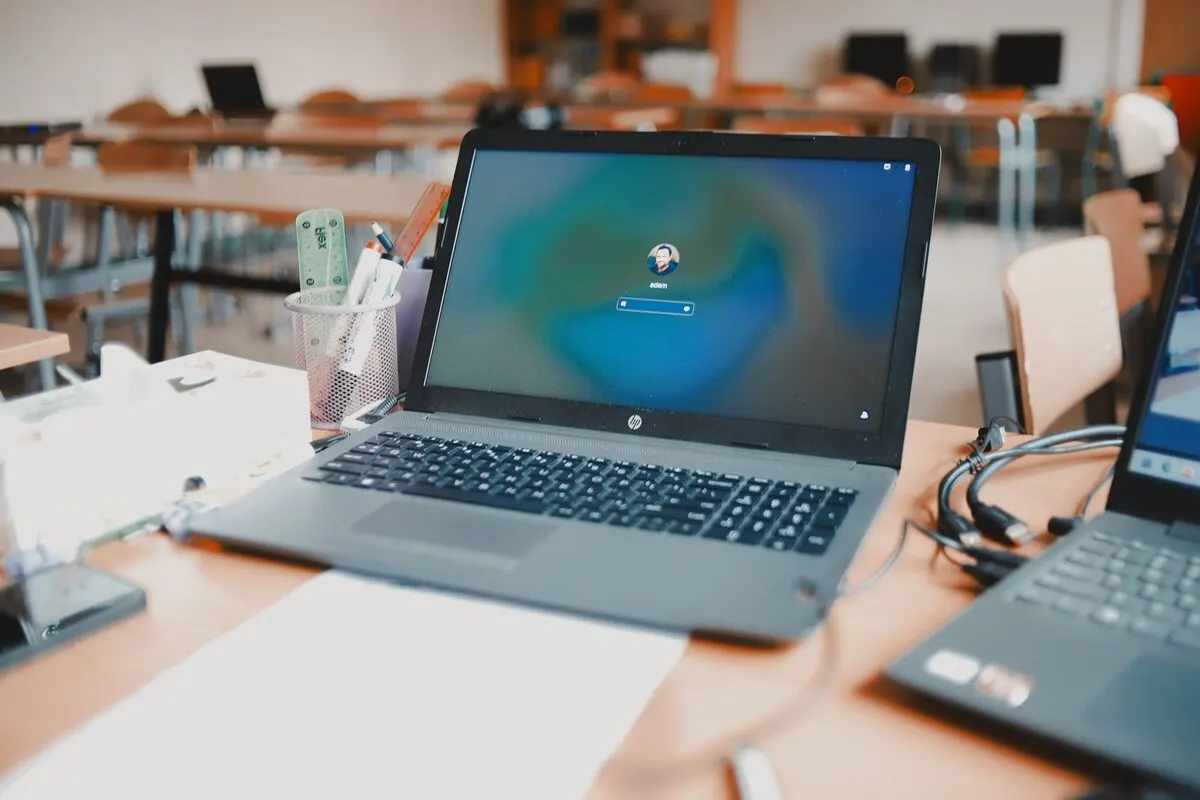 Laptop HP z ekranem logowania w pustej sali szkoleniowej z ławkami — Szkolenie z obsługi i zarządzania chatbotem AI na stronie firmowej